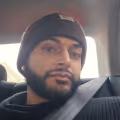 Ein Mann mit Bart und Hut sitzt auf dem Rücksitz eines Autos, abgebildet auf einem Foto von schlechter Qualität vor der Verbesserung von yourmove.ai