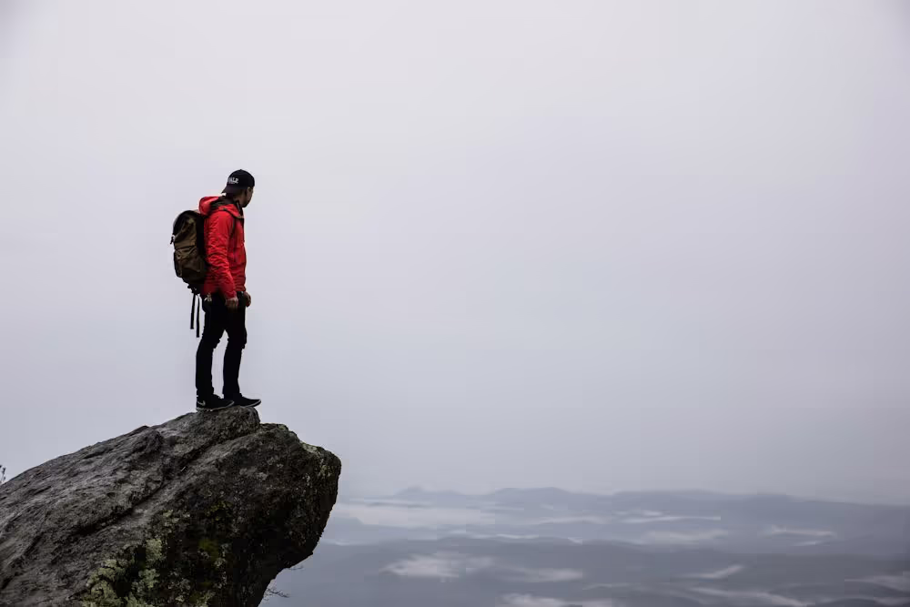 Man in a red jacket standing at the peak of a mountain